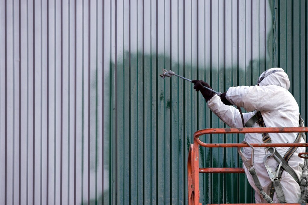 Painter in protective gear refinishing a commercial building exterior from a lift